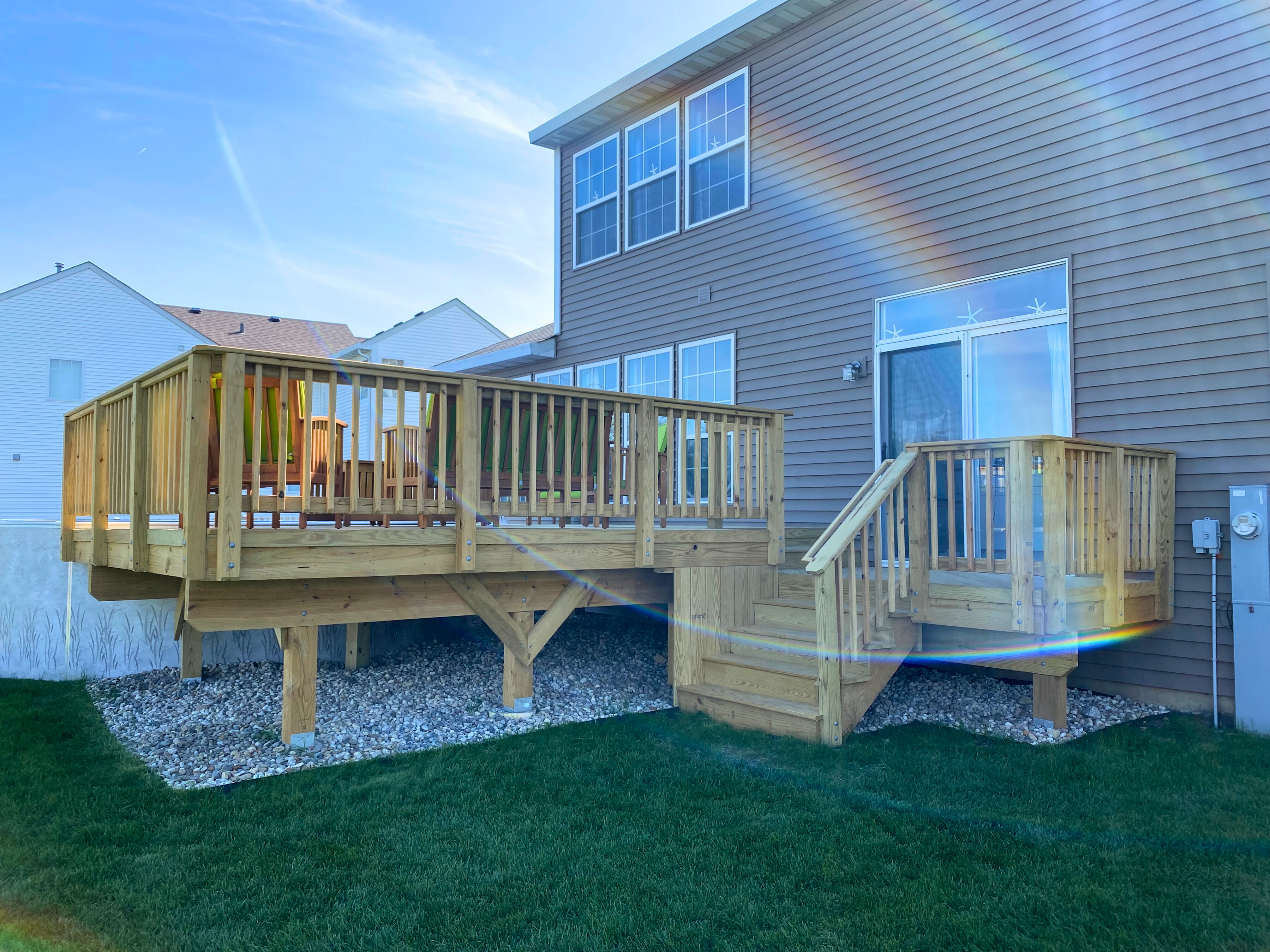 Newly built custom wood deck with stairs and railing on the back of a light brown house in Mundelein, IL.