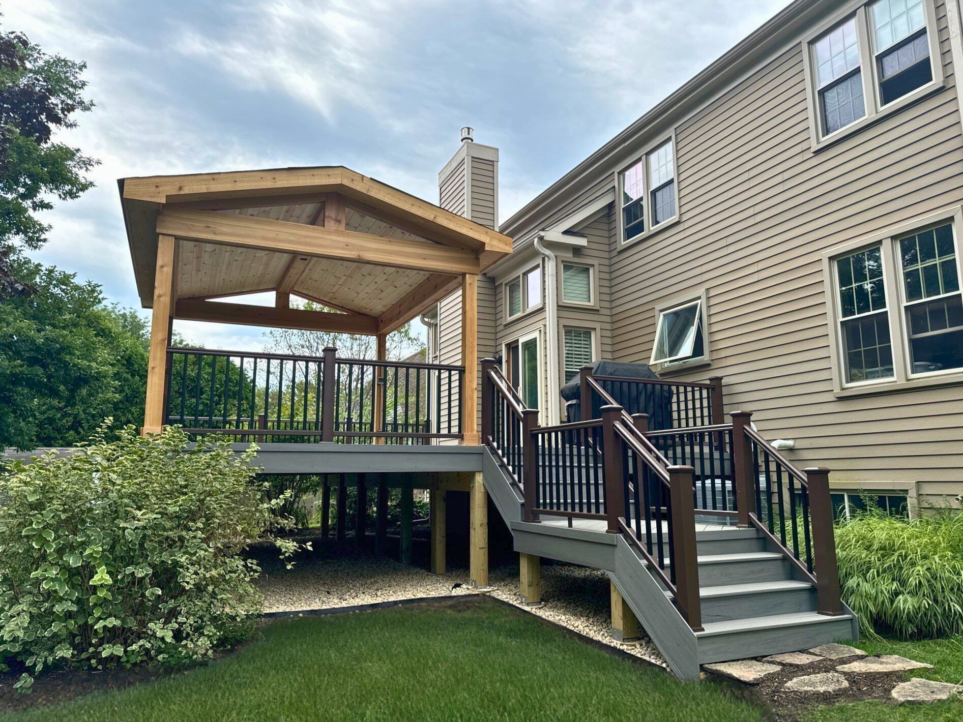 Deck and covered porch addition to a tan house in Mundelein, IL, with dark composite decking and black railings.