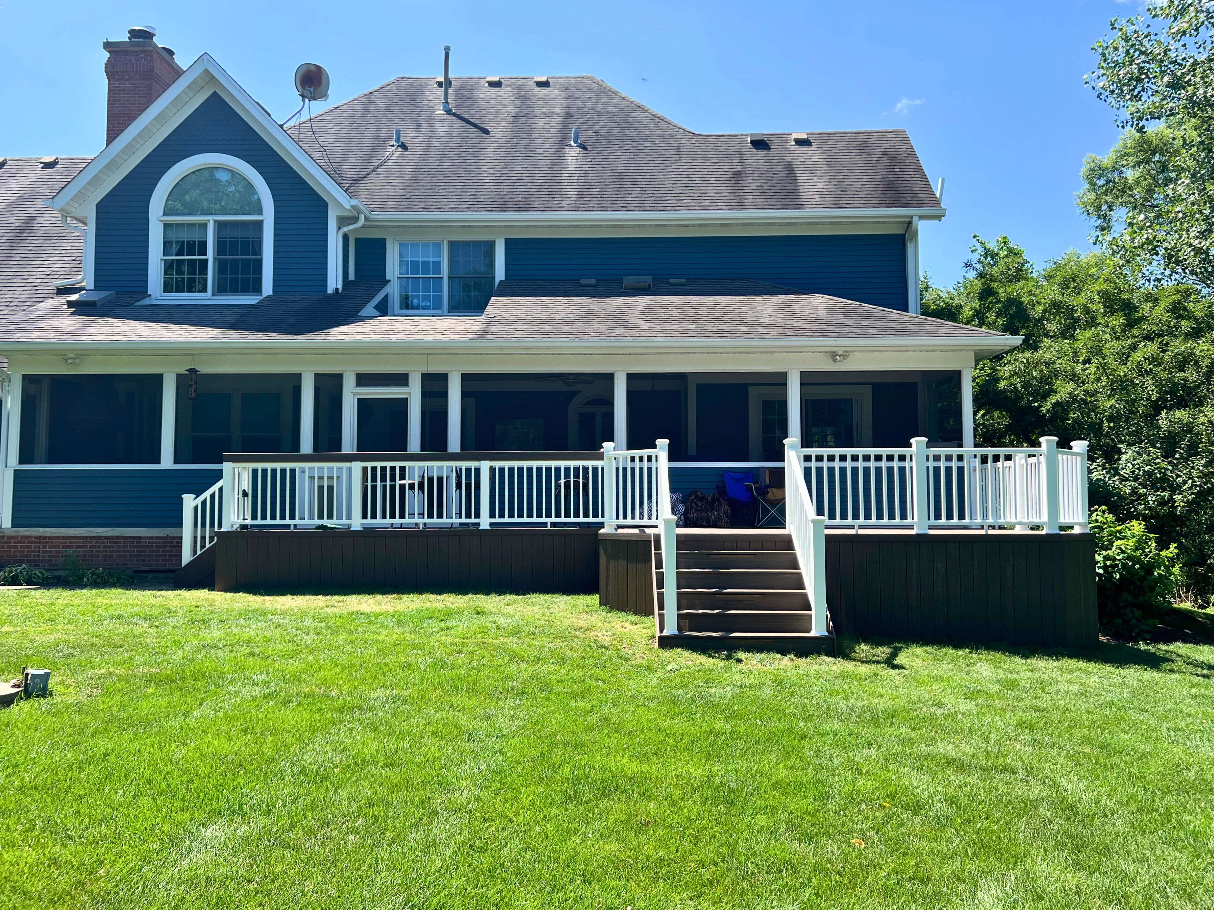 Large multi-level deck with white railings and a screened porch on the back of a blue house in Mundelein, IL, overlooking a green lawn.