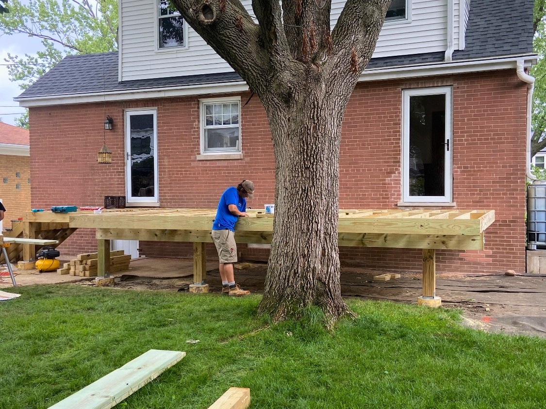 man working on building a wood deck off of a brick house