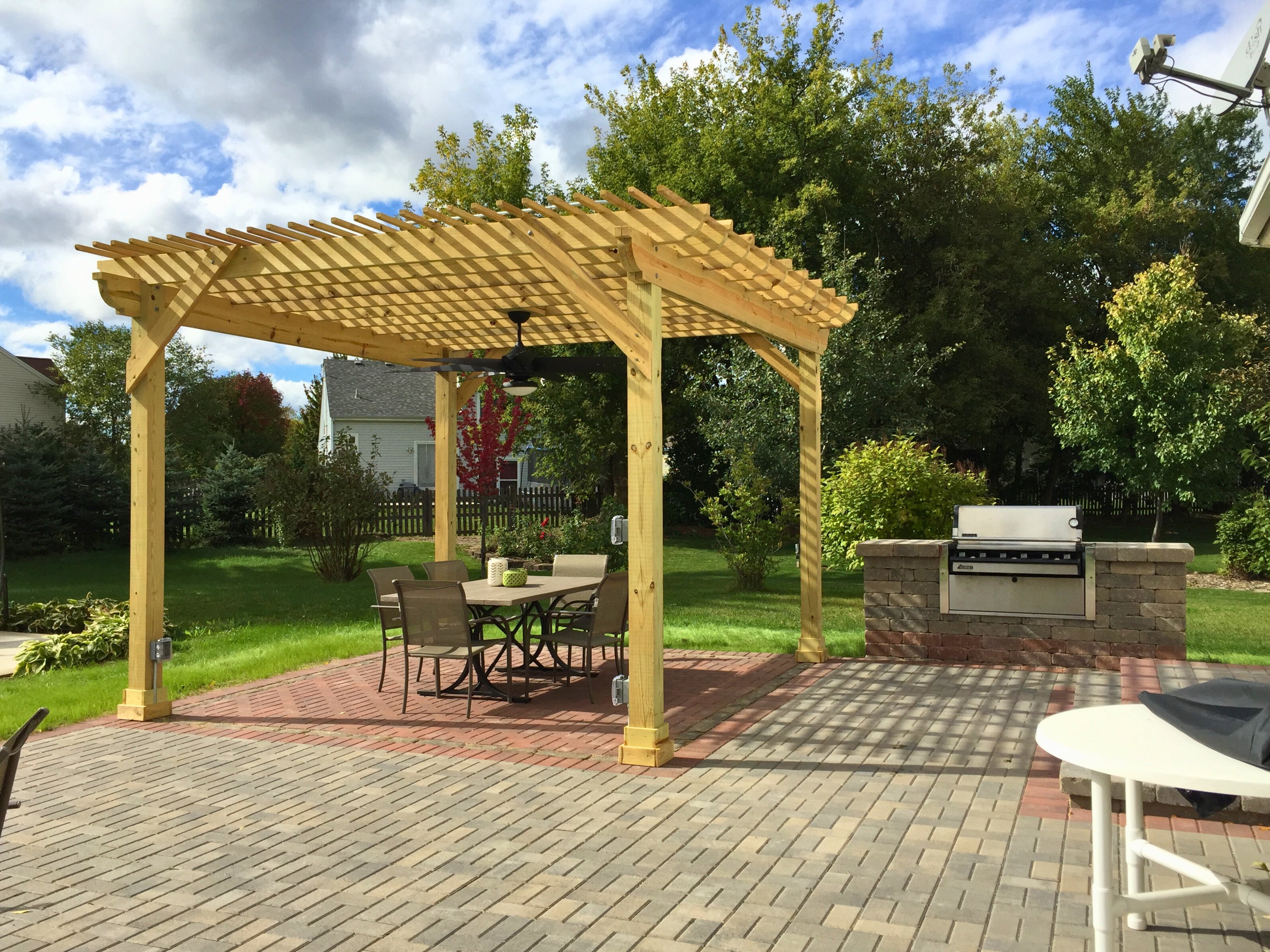 Custom-built wooden pergola over a brick paver patio in Gurnee, featuring an outdoor kitchen grill station and dining area.