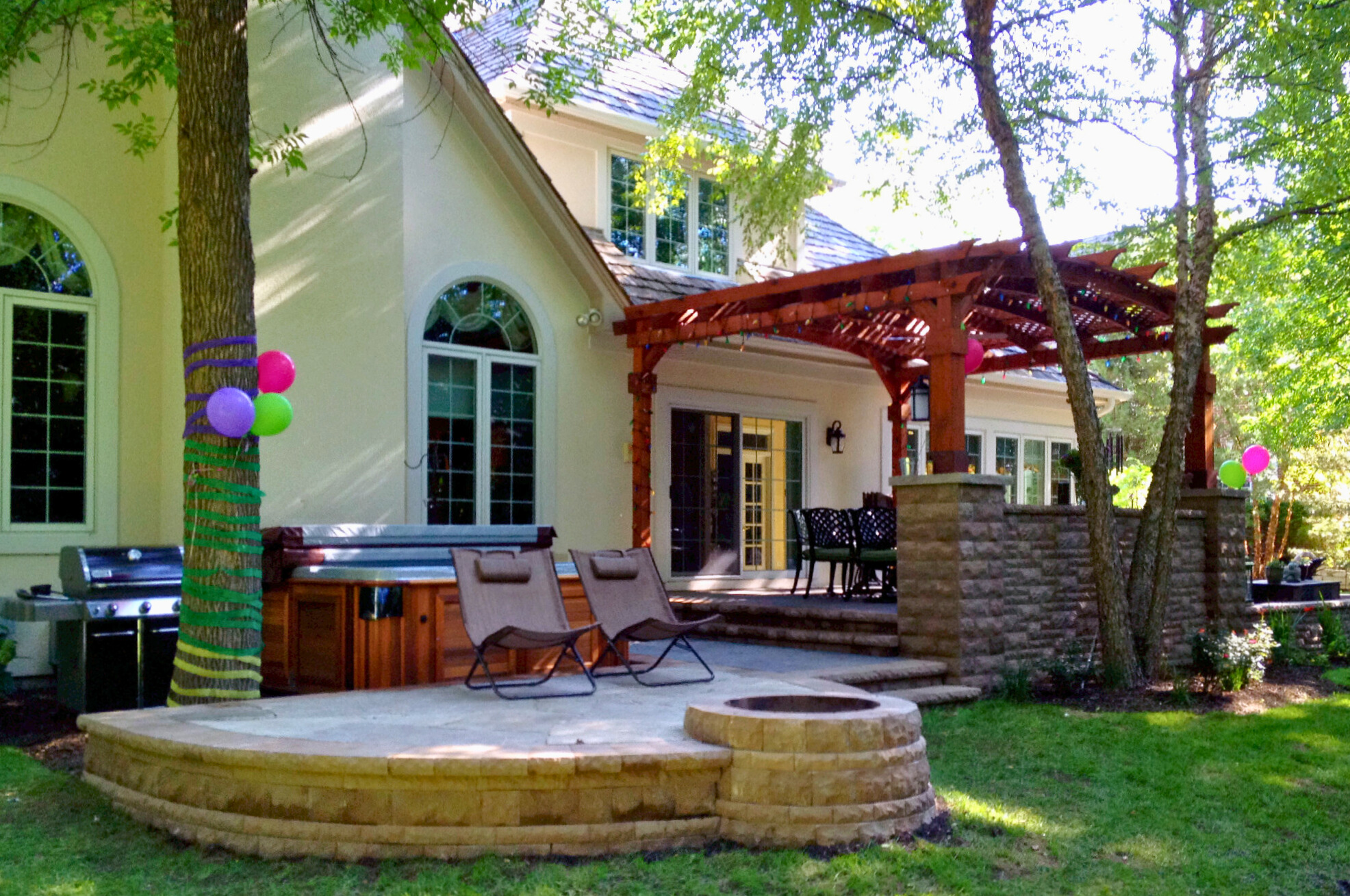 Custom patio with stone details and a reddish-brown wooden pergola next to a house in Libertyville IL.