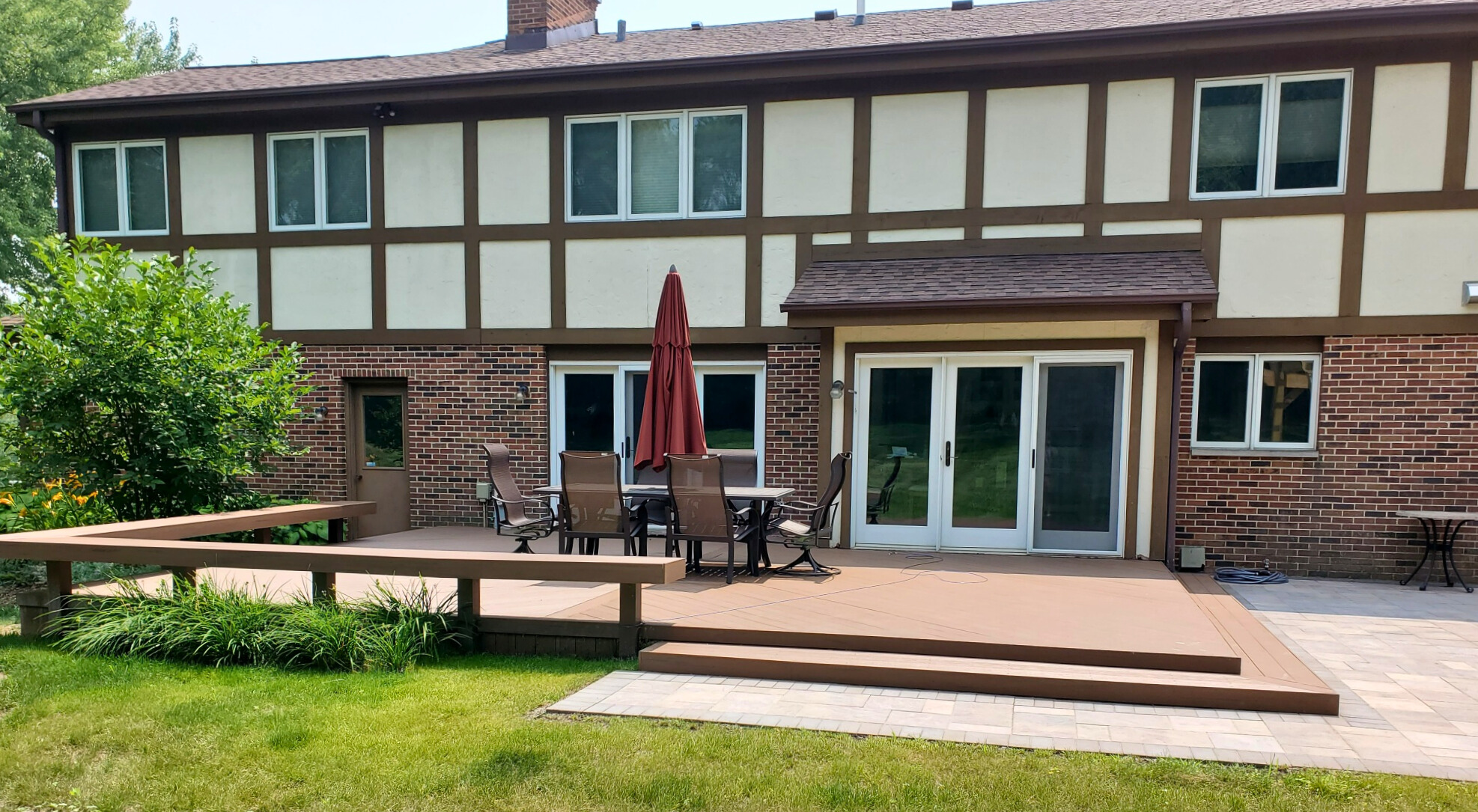 Low-profile platform composite deck with a long railing, connecting to a paver patio and a house with brick and stucco siding in Mundelein, IL.