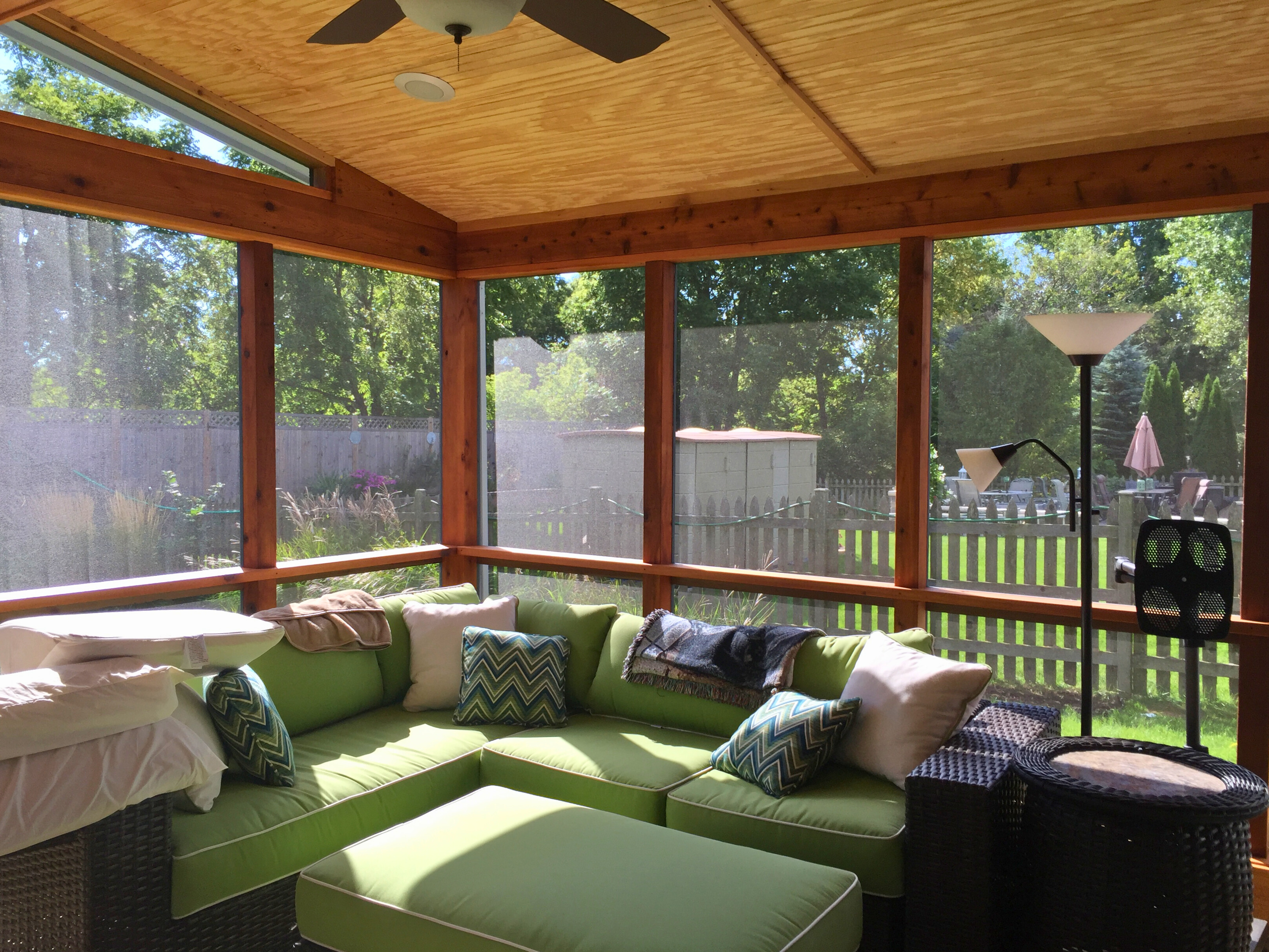 Interior view of a cozy screened porch in Gurnee with a natural wood ceiling, ceiling fan, and comfortable green sectional seating.