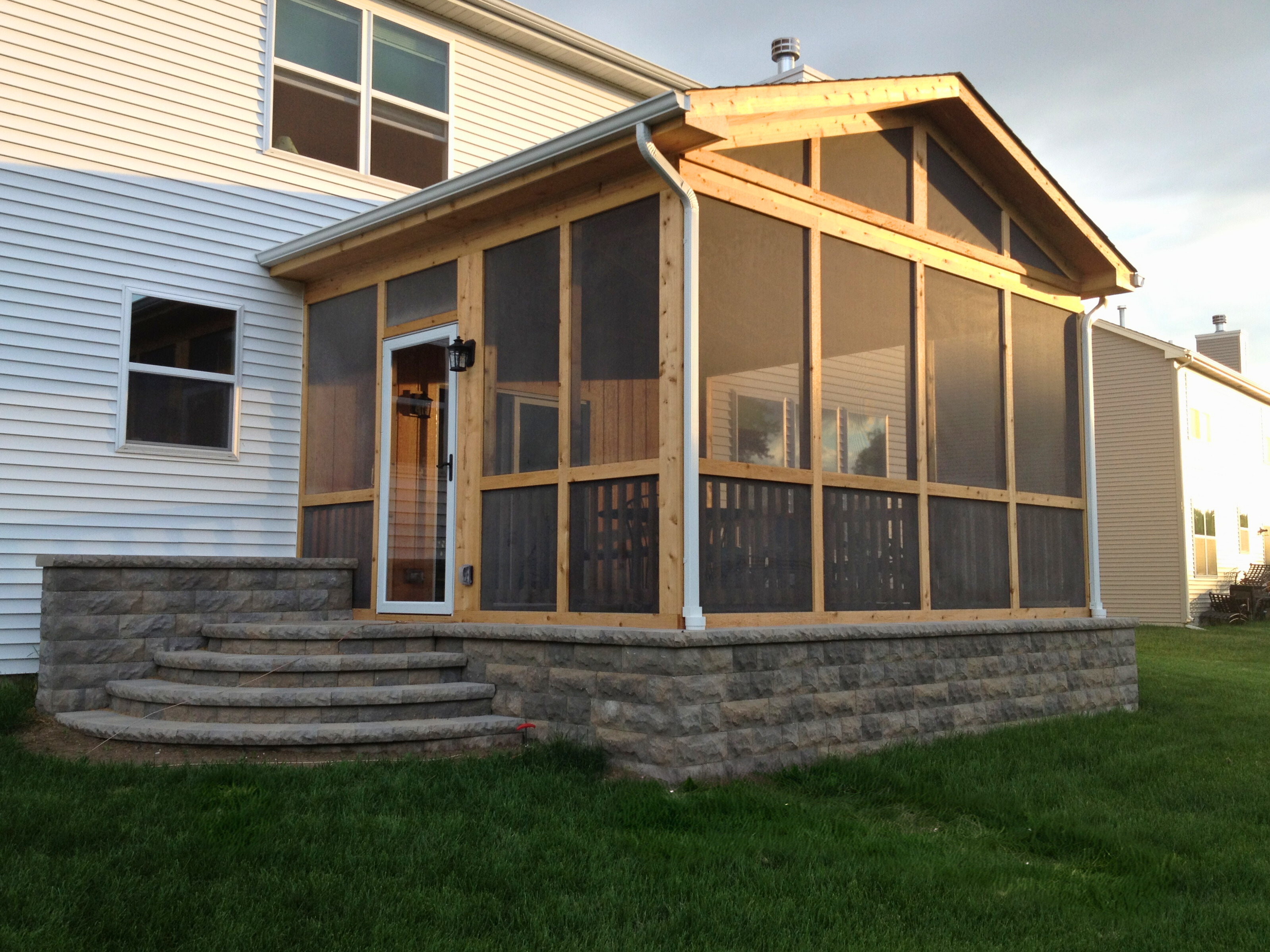Newly constructed screened porch with a stone foundation and wood framing, attached to a white house in Mundelein, IL.
