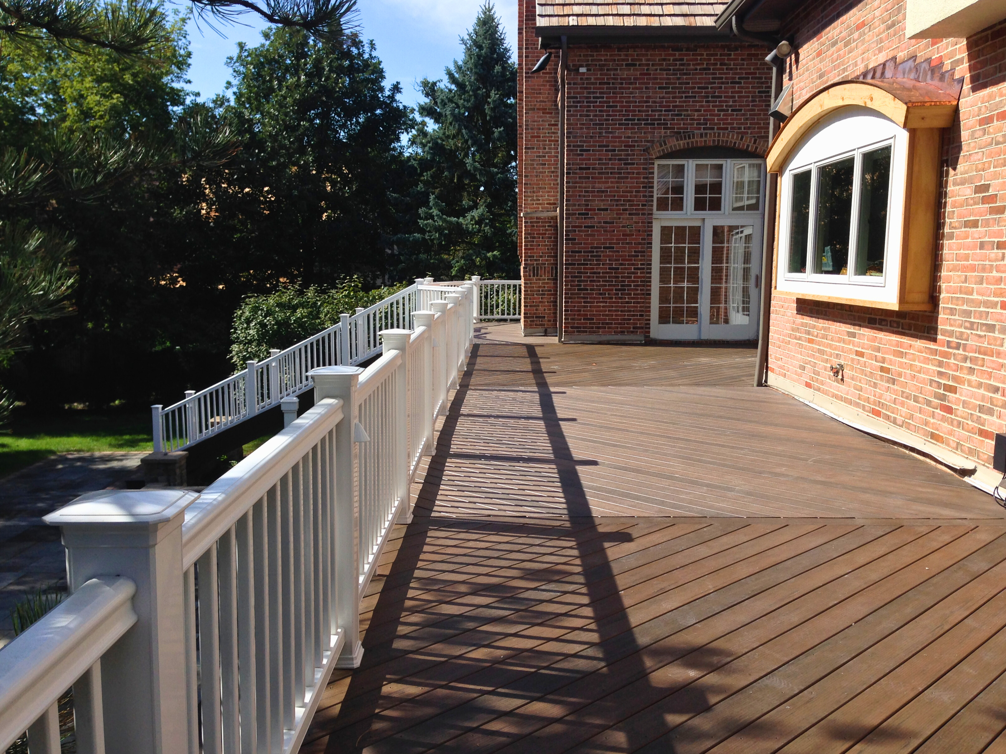 Expansive brown composite deck with white railing extending around a brick house, Barrington, IL.