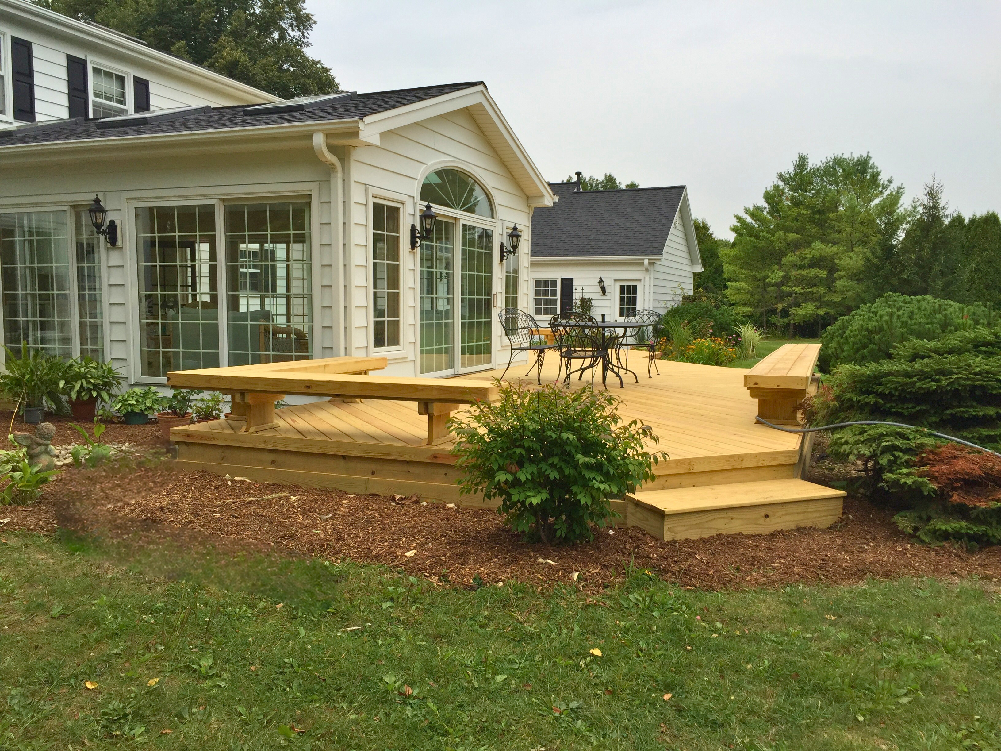 A charming wood deck with integrated benches extends from a bright sunroom