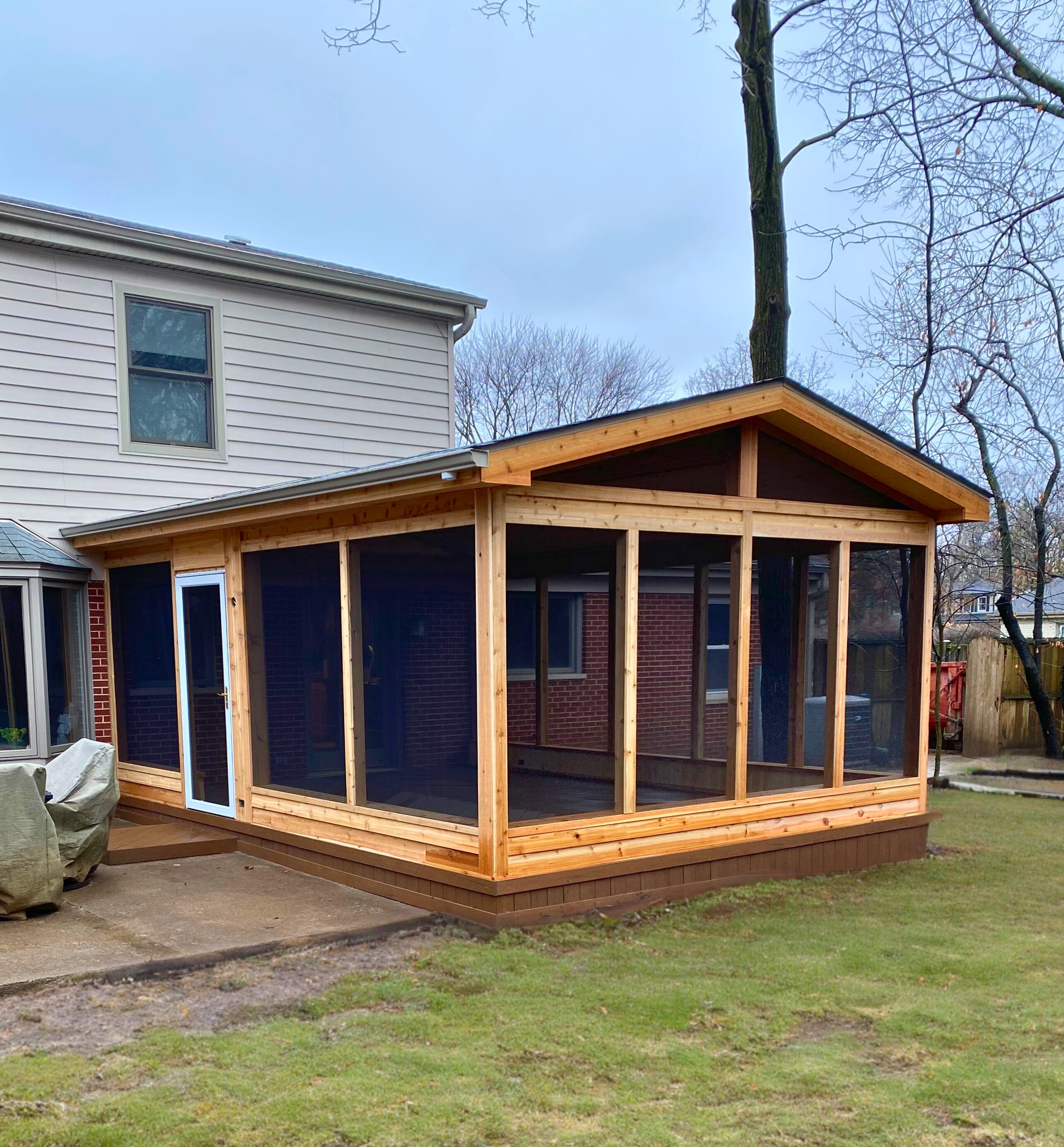 A newly constructed wooden screened porch with a gabled roof, attached to a light-colored home in Deerfield, IL, visible from the backyard.