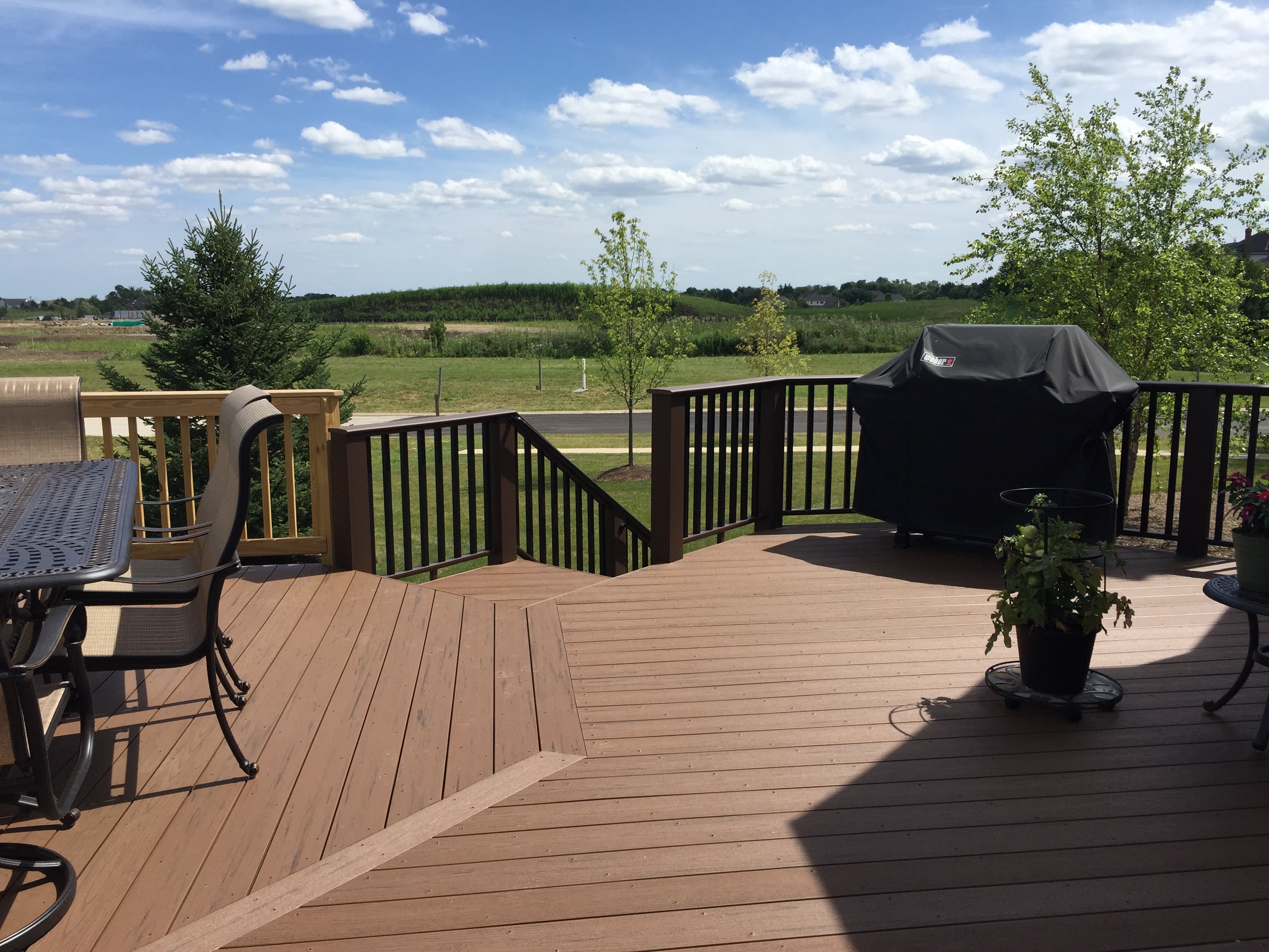 A light-colored wooden deck with black balusters and a lattice skirt, built against the side of a house, with stairs leading down to a grassy yard in Hawthorn Woods, Illinois.