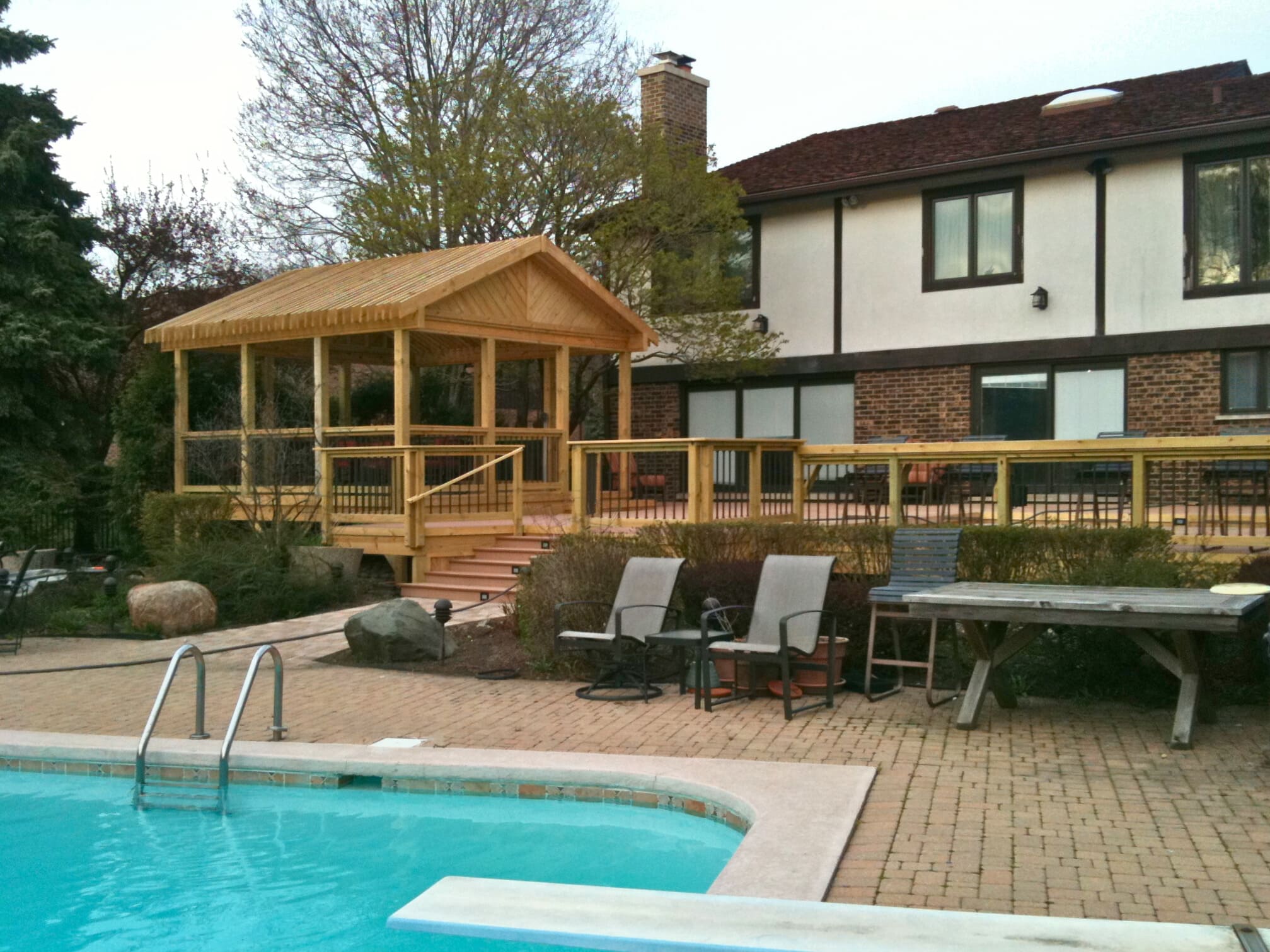 Large wooden deck with a covered pergola and adjacent paver patio and swimming pool in Highland Park, IL