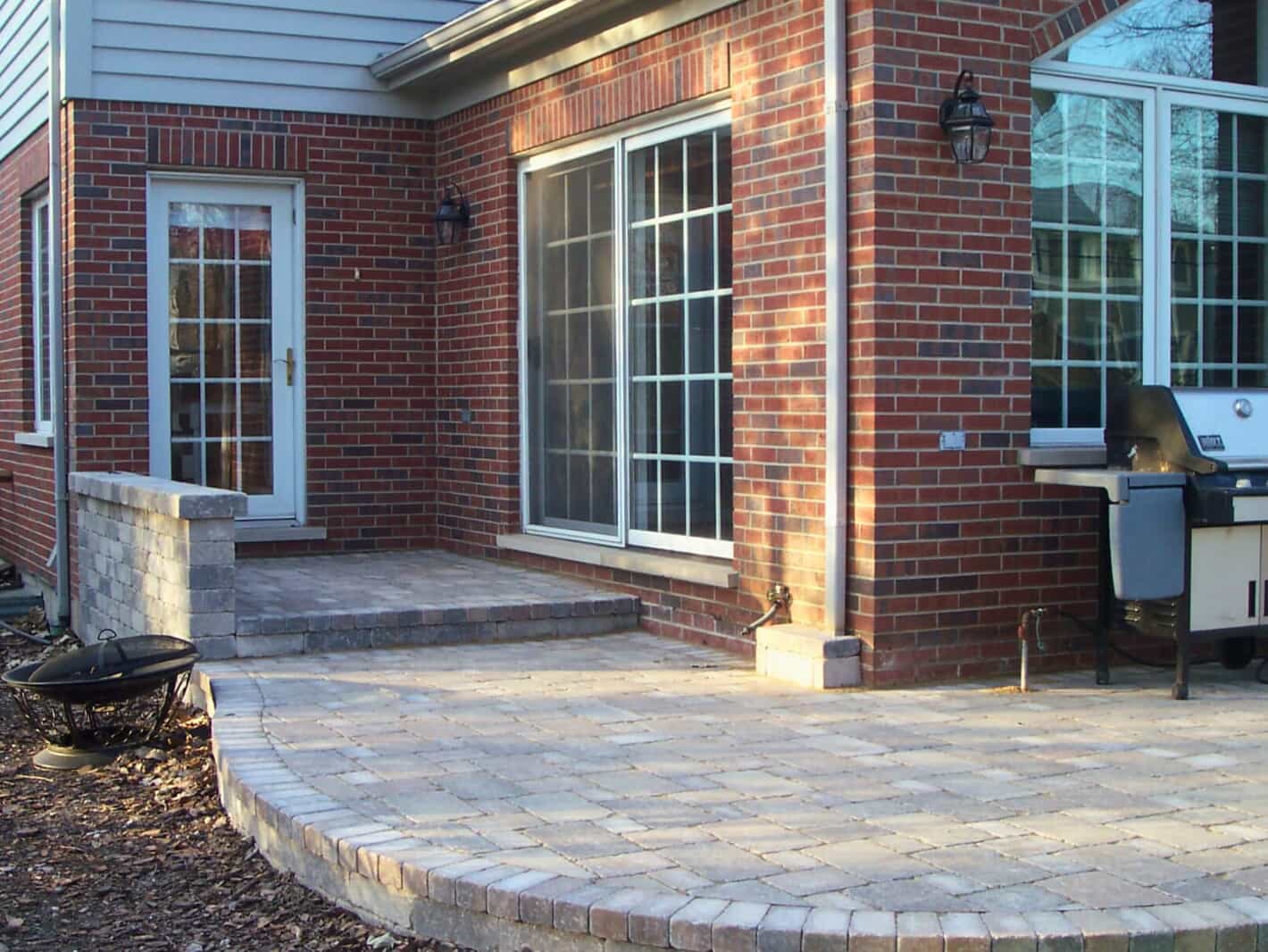 Curved brick paver patio with retaining wall next to a red brick home in Highland Park, IL