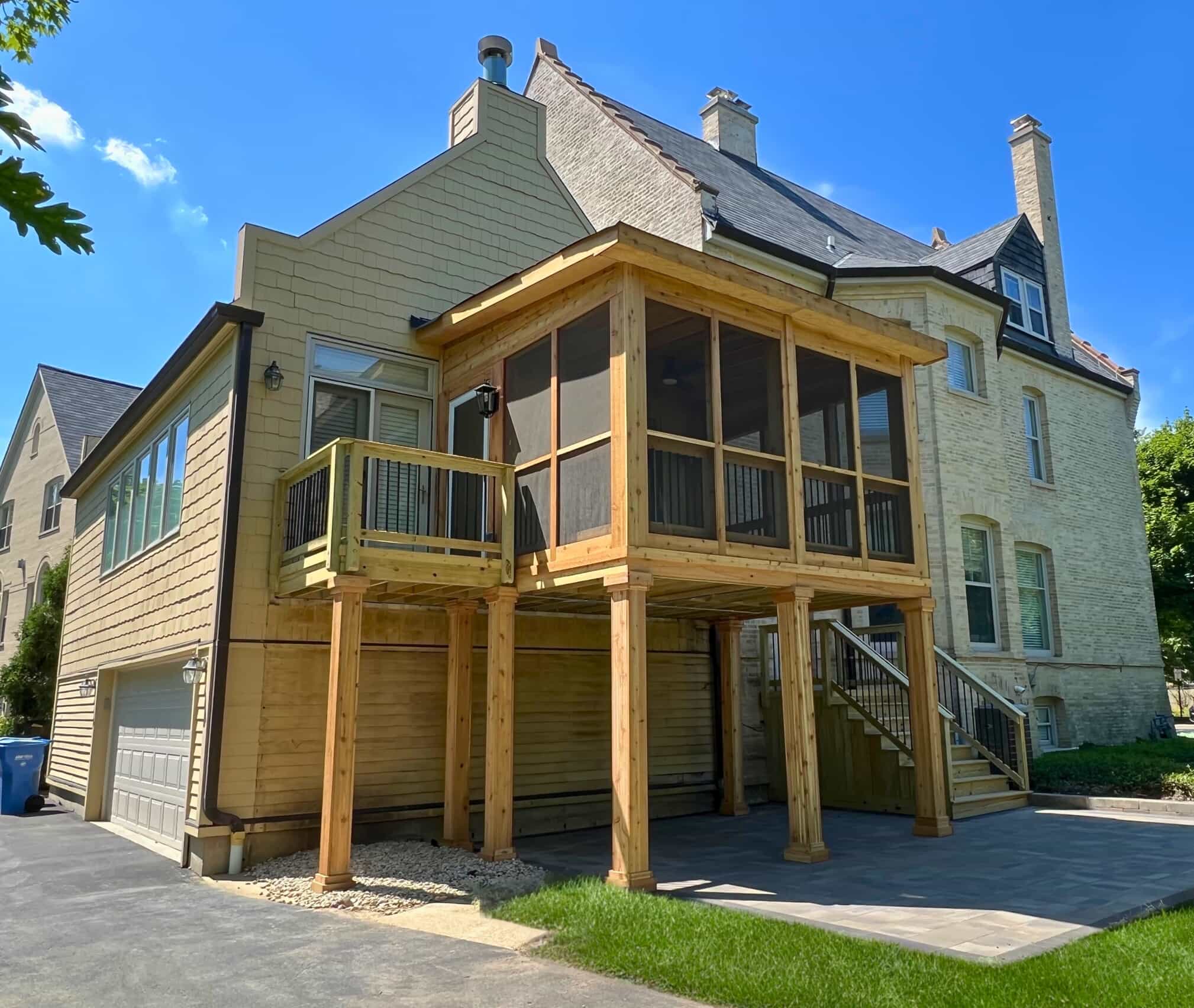 Elevated custom screened porch with wood and black railings overlooking a paver driveway in Highland Park, IL