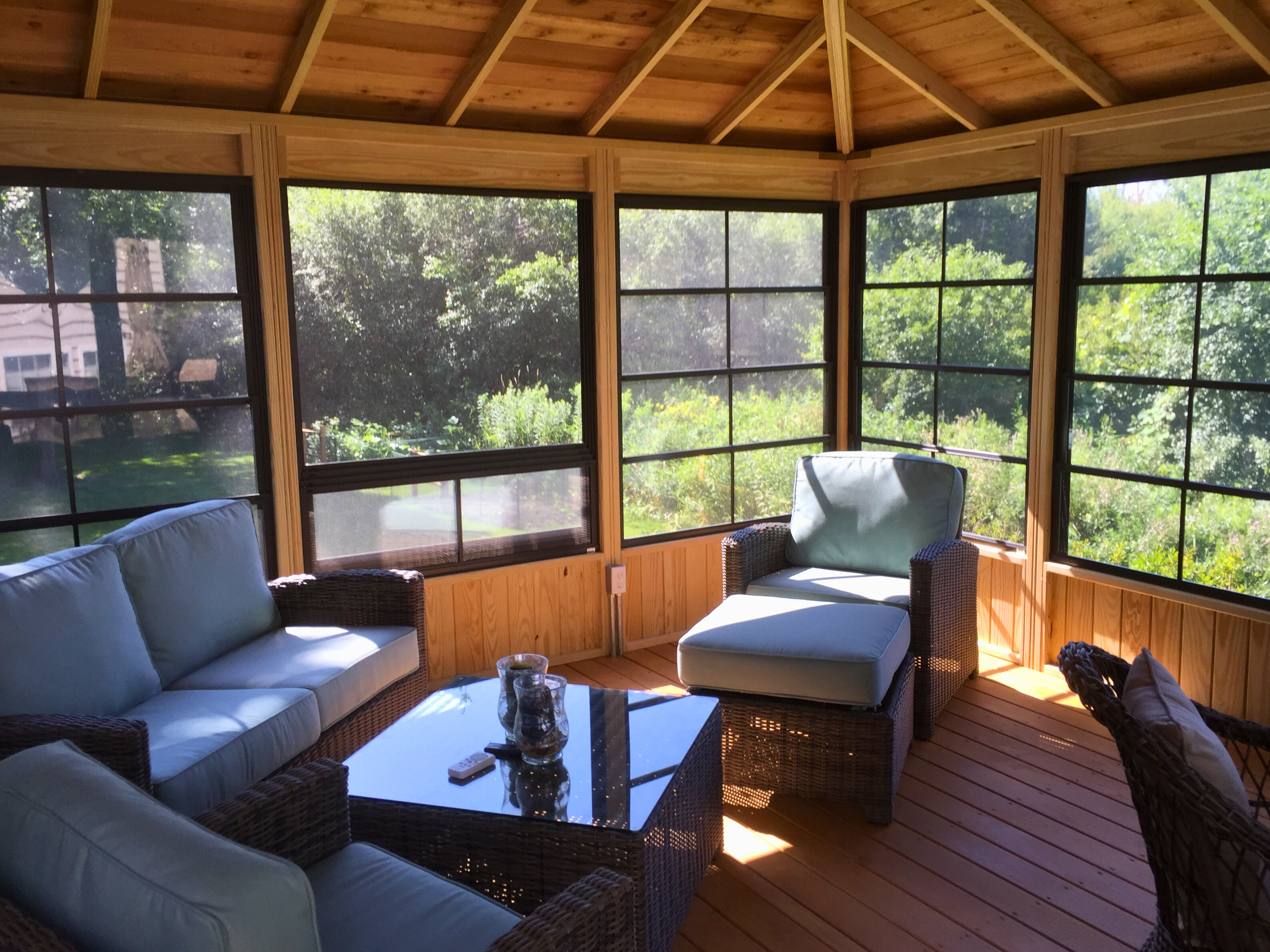 Interior view of a three-season room in Mundelein, IL, with wood walls and ceiling, large windows, and comfortable patio furniture.