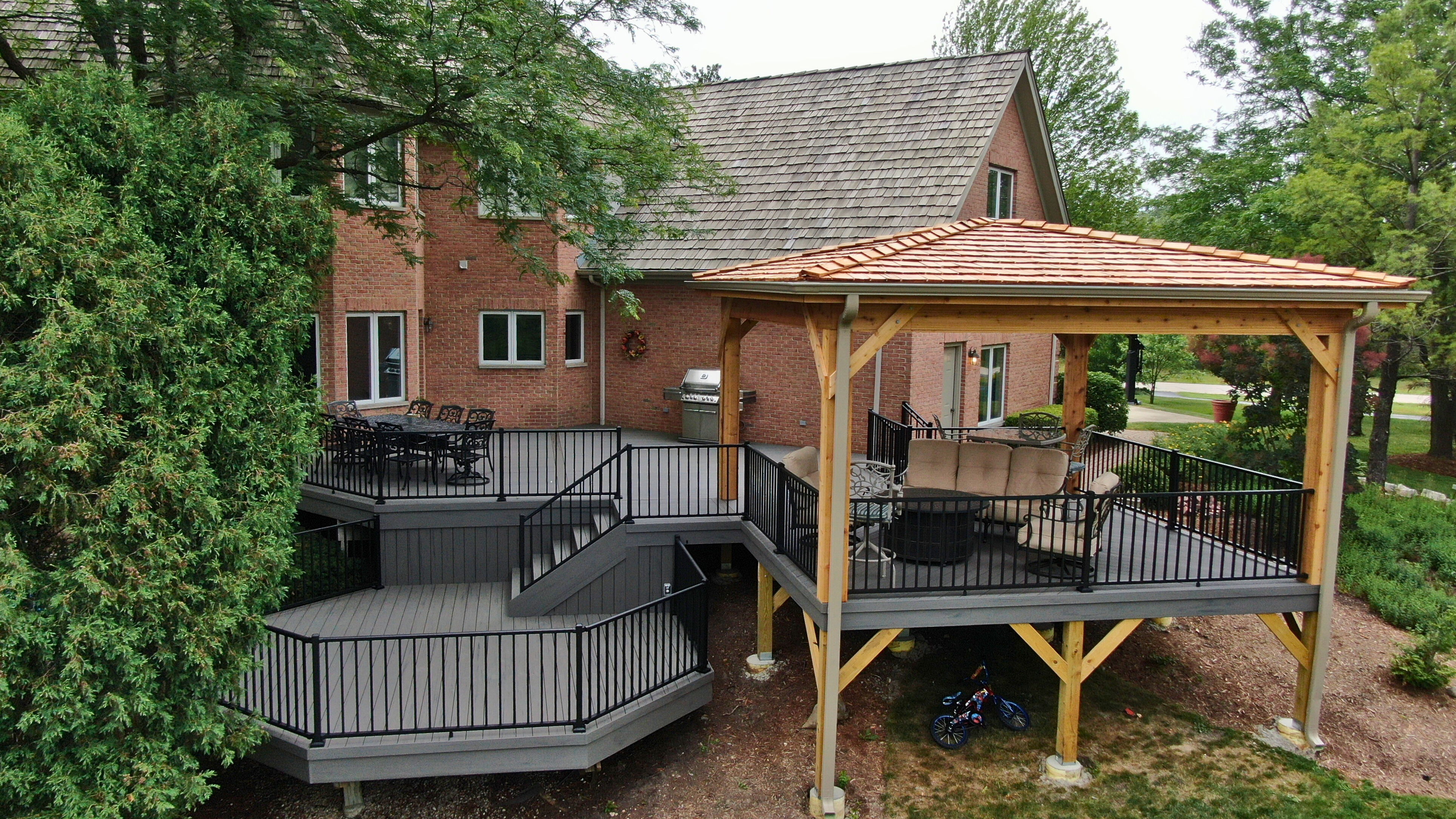 Multi-level TimberTech composite deck with black railings and a custom wood pergola attached to a brick house in Mundelein, IL.