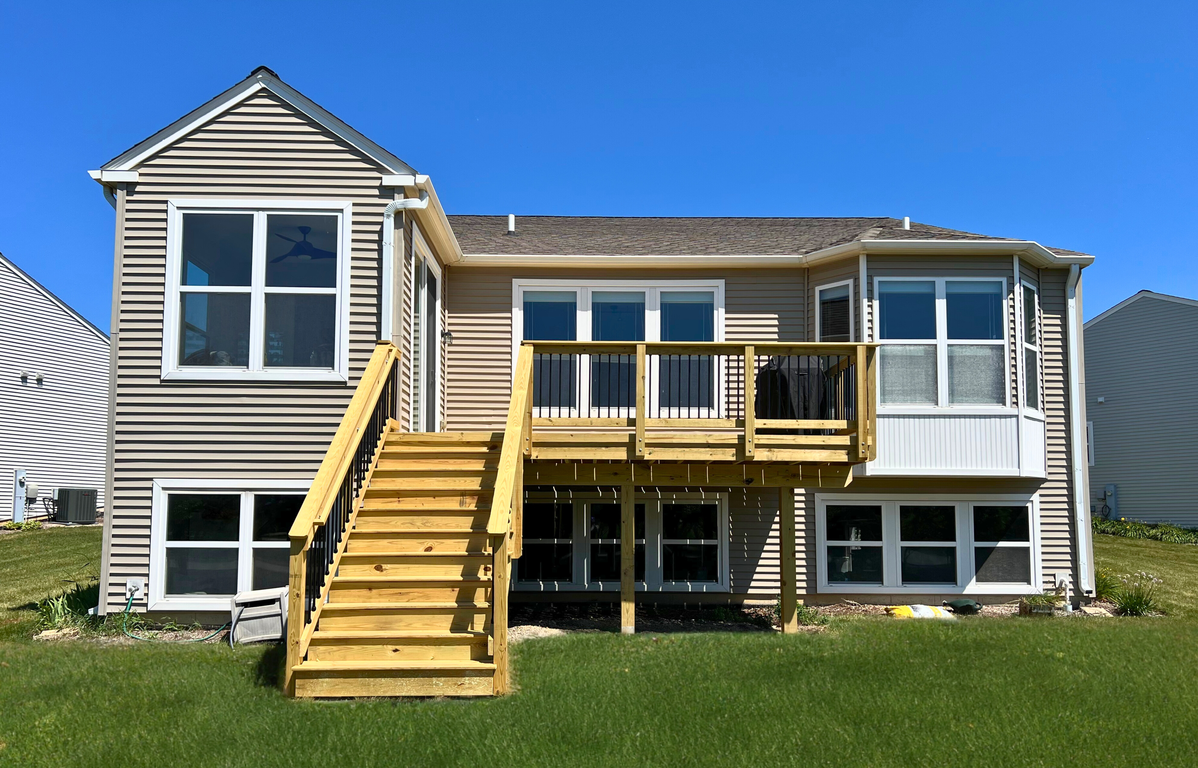 Newly built wood deck with stairs and black metal railings on the back of a tan siding house in Mundelein, IL.