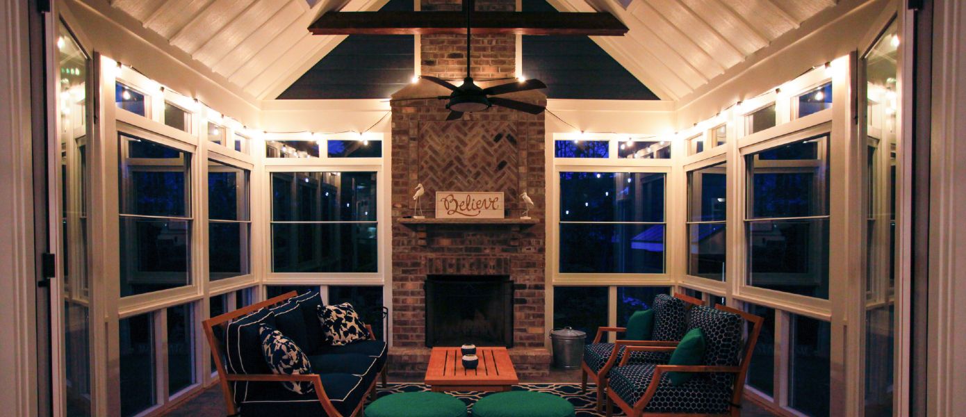 Furnished sunroom with fireplace and fan lit with patio lights.