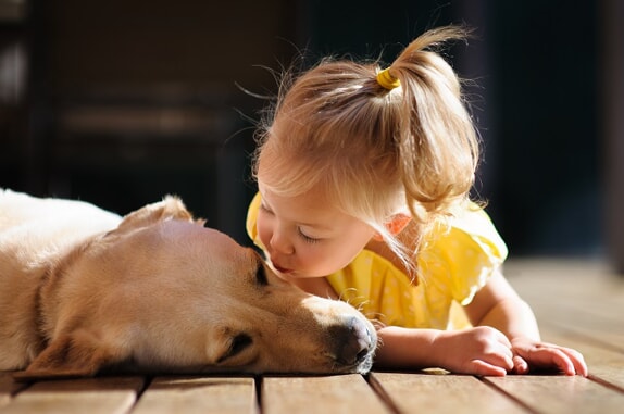 little girl giving her dog a kiss on a deck