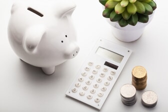 white piggy bank next to calculator and stacks of coins 