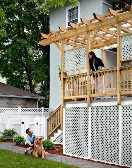 Woman speaking to man and dog below from raised deck with pergola