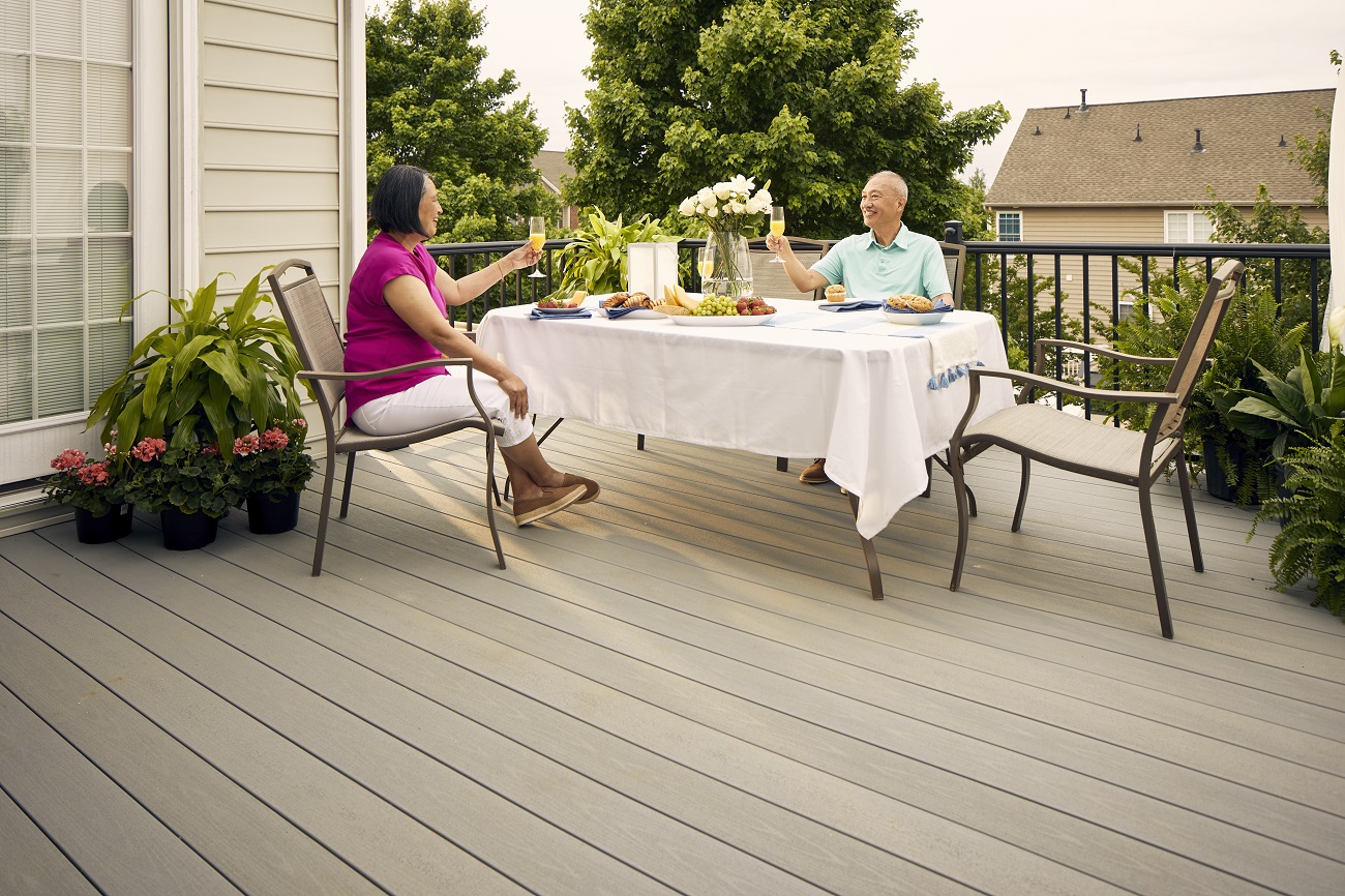Two individuals have a meal outside on their deck and toasting to one another.