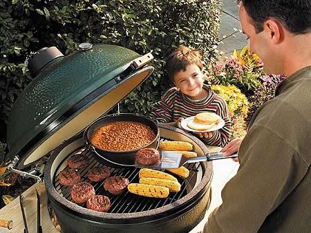 man cooking on a green egg ceramic cooker as his son watches