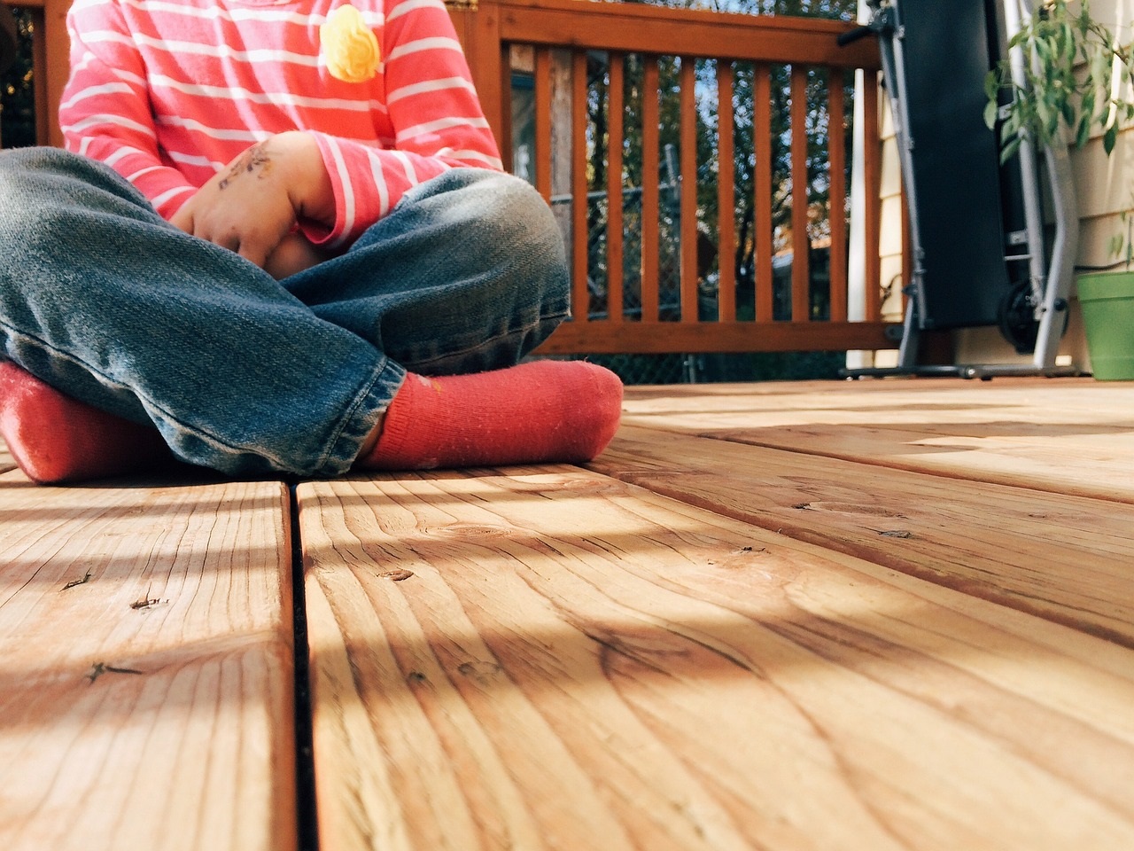 Child wearing jeans and red socks sitting on wooden deck
